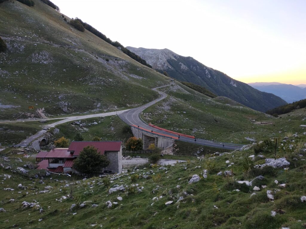 Valle con la strada del valico, un rifugio rosso e prati verdi al tramonto
