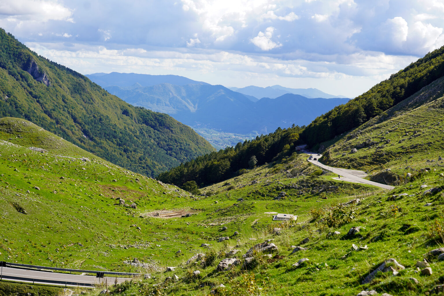 Tornanti della strada del valico tra prati verdi, con la valle in lontananza