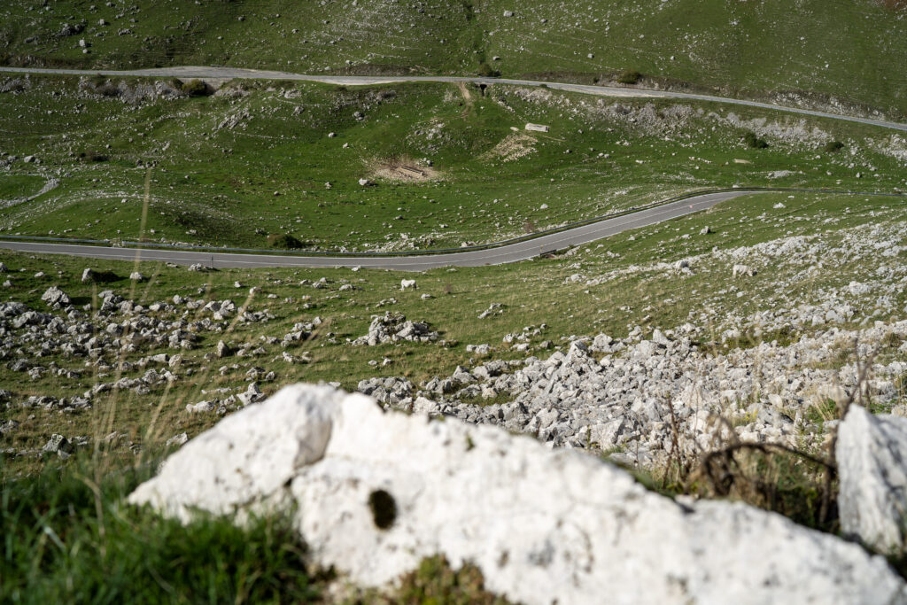 Strada del valico che attraversa i prati, con grandi rocce bianche in primo piano