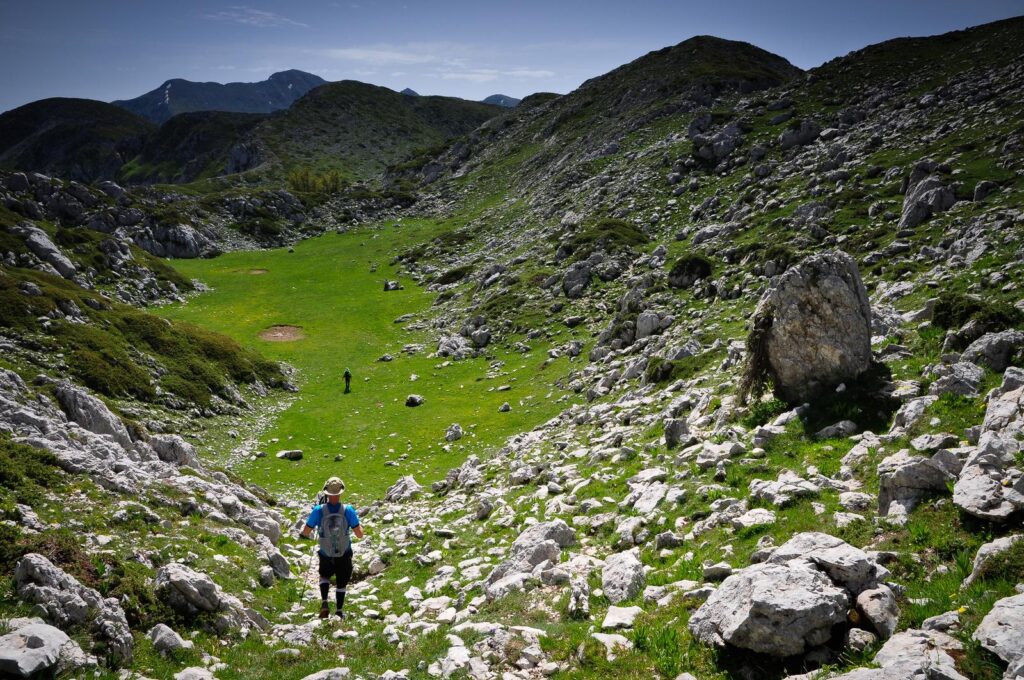 Escursionista in una conca erbosa tra rocce e pendii di montagna
