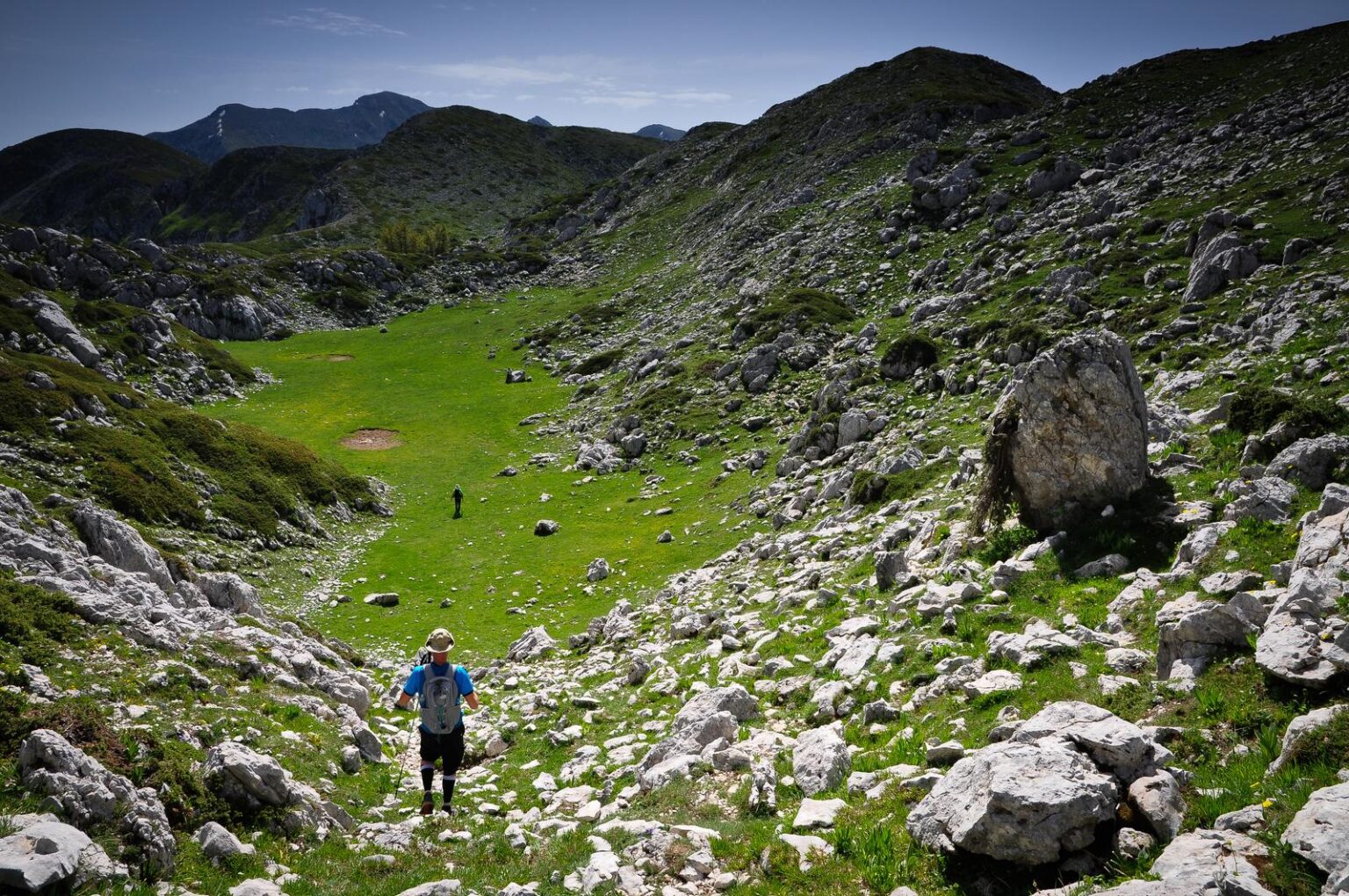 Escursionista in una conca erbosa tra rocce e pendii di montagna