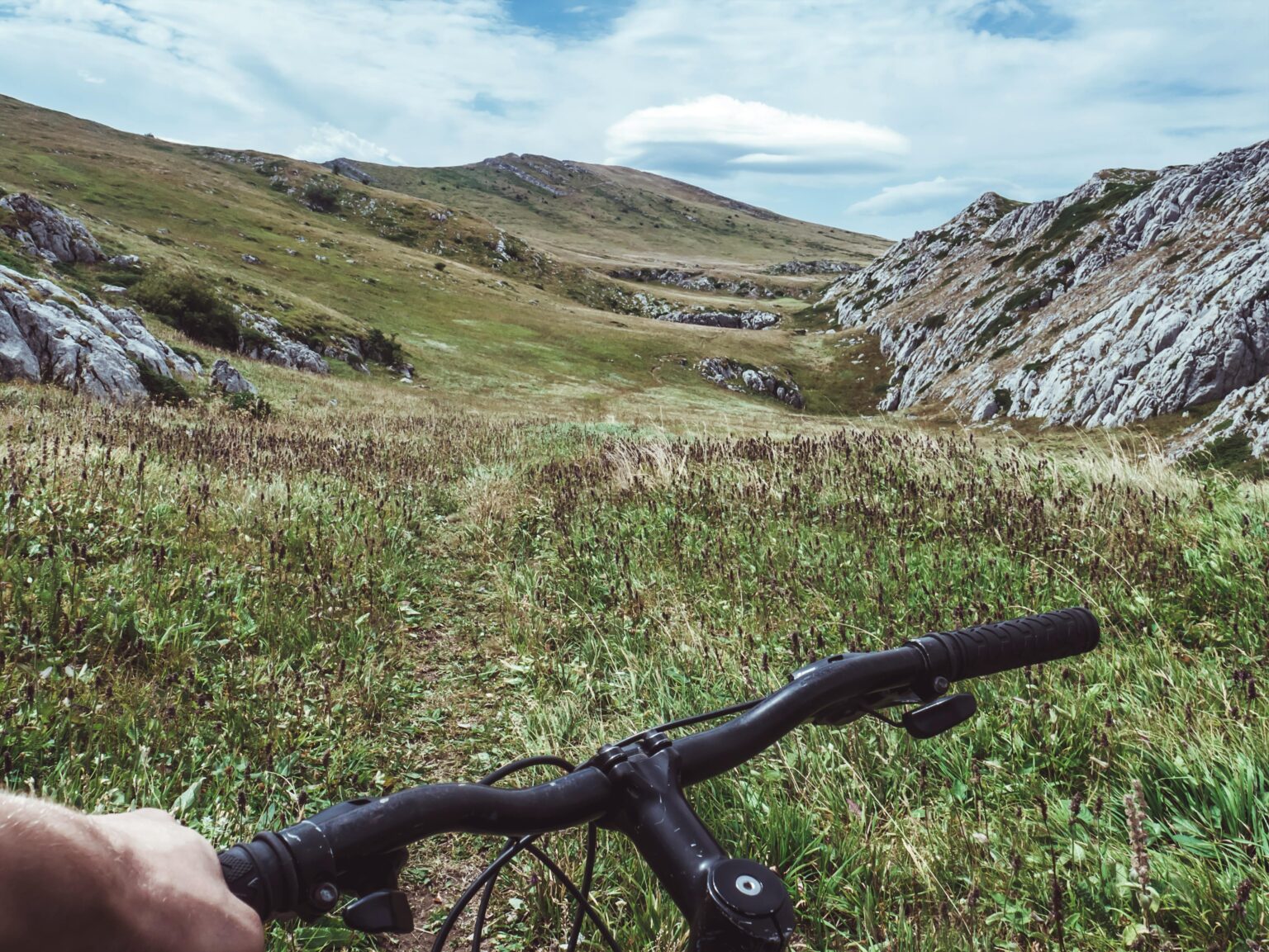 Handlebars of a mountain bike on a high-altitude meadow, with rocks and a cloudy sky