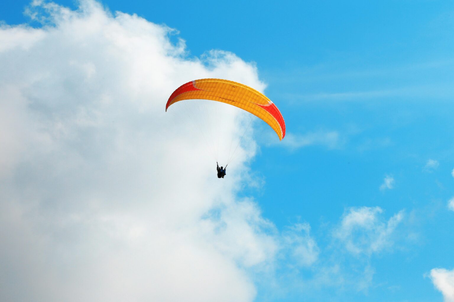 Paragliding with an orange and yellow sail among the clouds