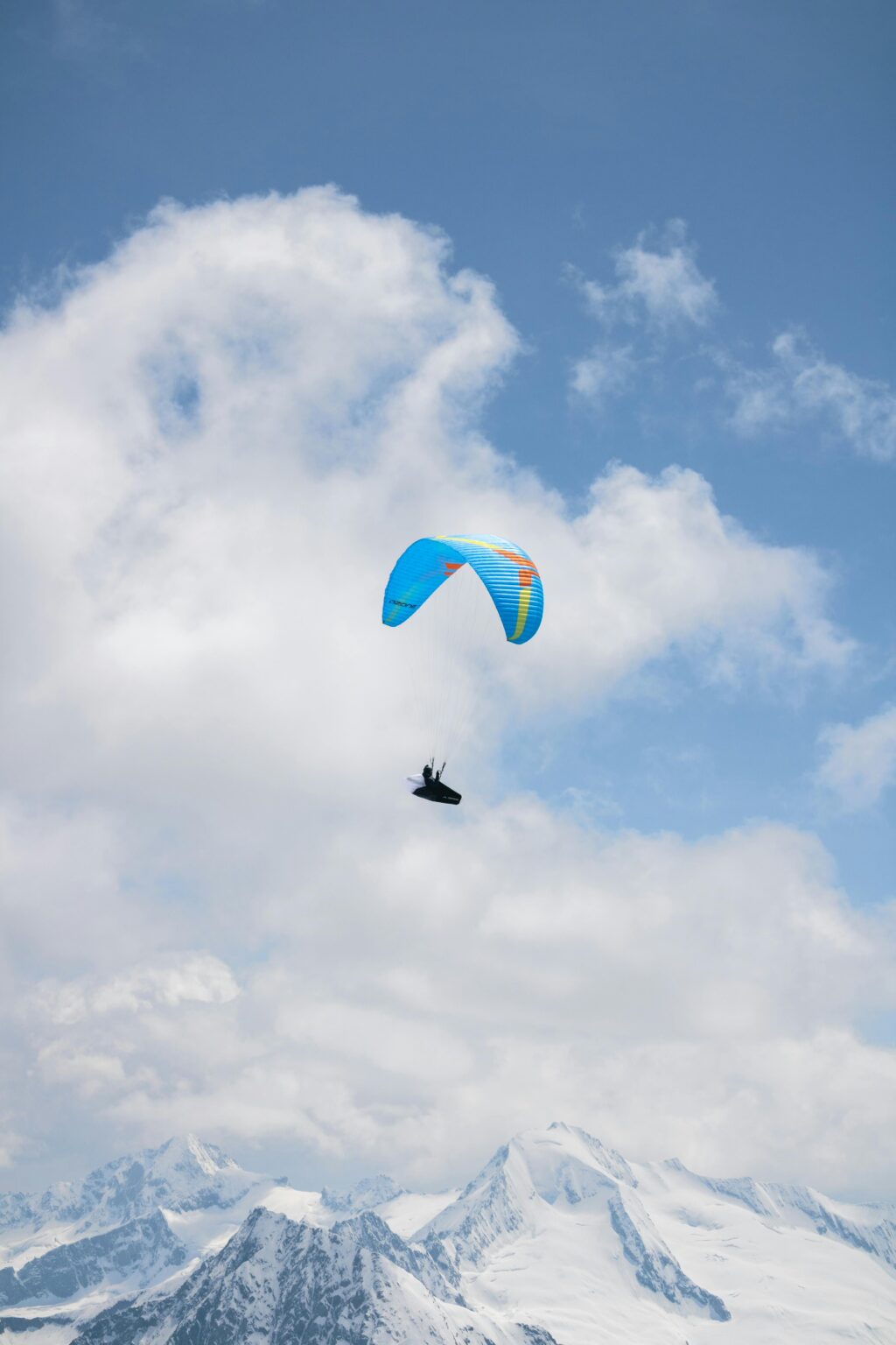 Blue paragliding among the clouds above snow-capped peaks