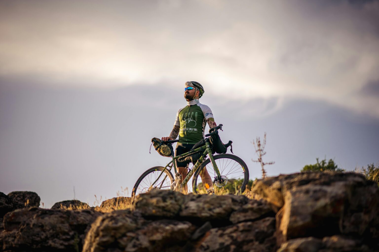 Cyclist with road bike on a rock top, under a cloudy sky
